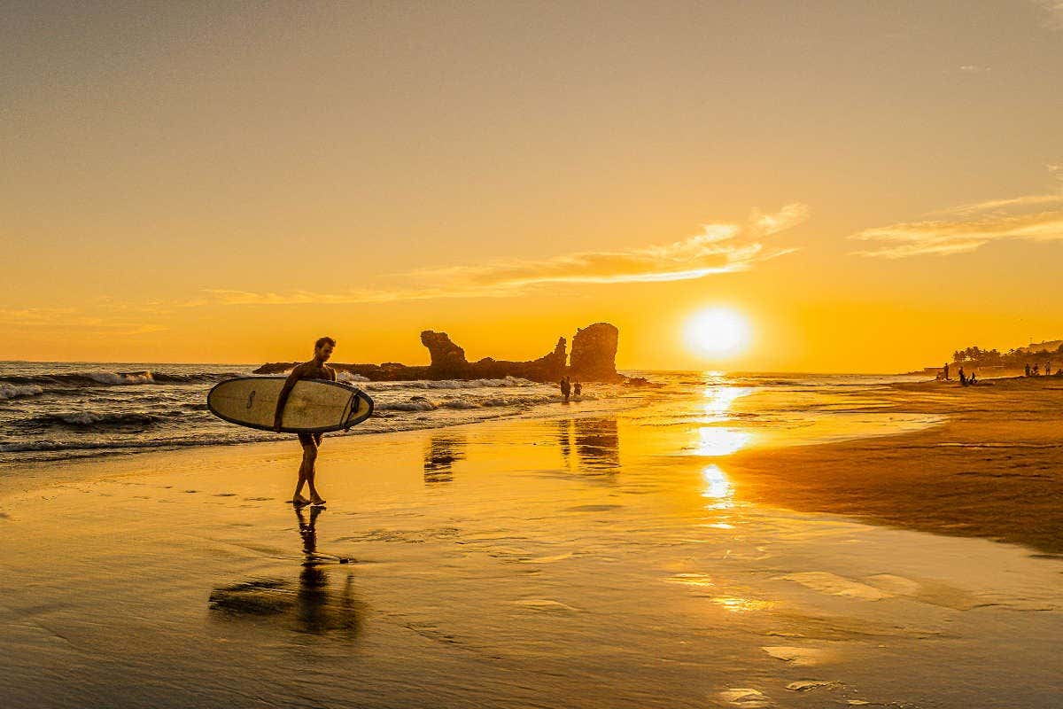 Un hombre con una tabla de surf en una playa al atardecer