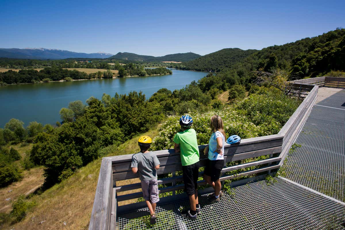 Tres personas con casco de ciclistas observan desde el mirador de Garaio el embalse de Ullibarri-Gamboa