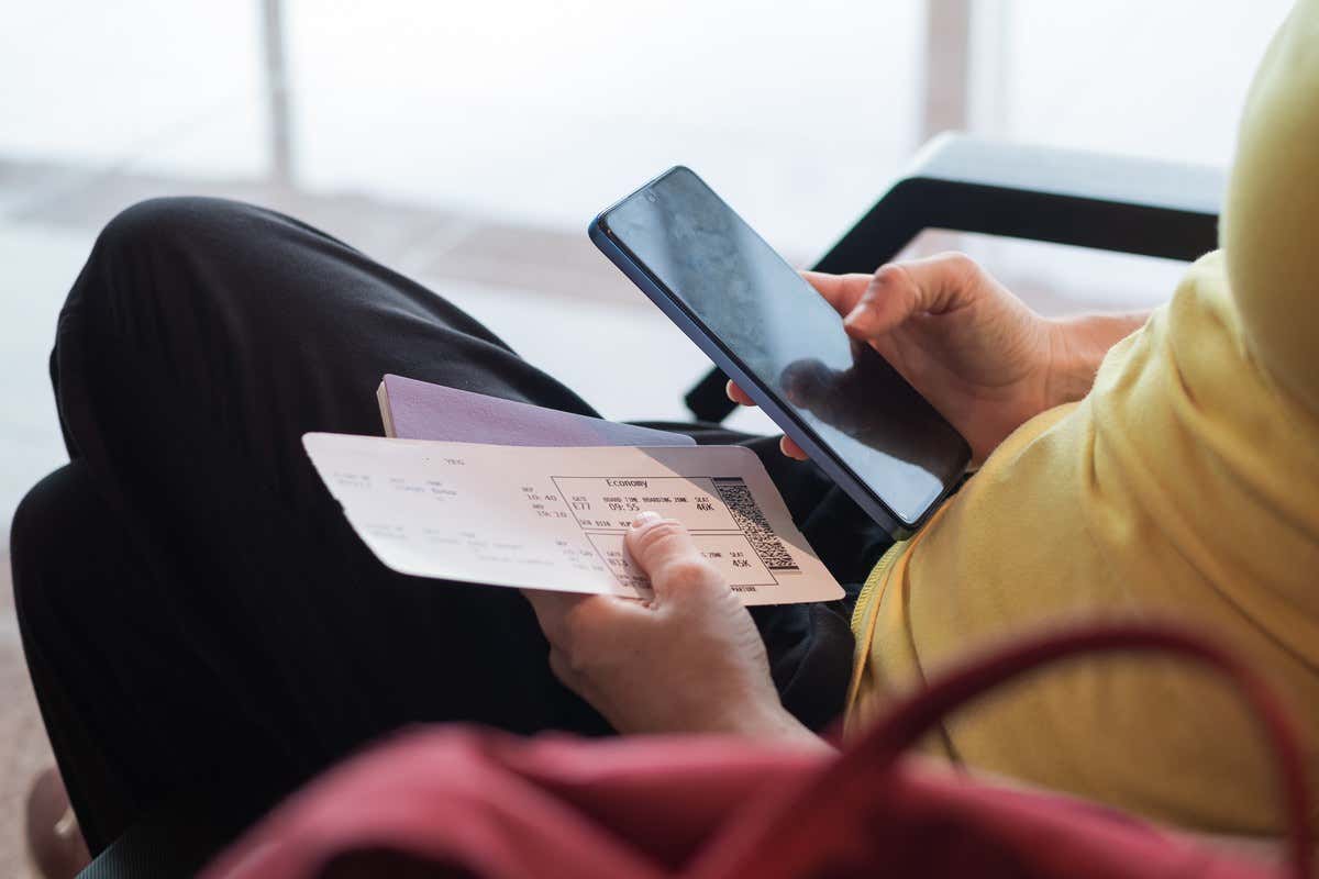Un pasajero sostiene la tarjeta de embarque y el pasaporte mientras consulta el teléfono antes de volar