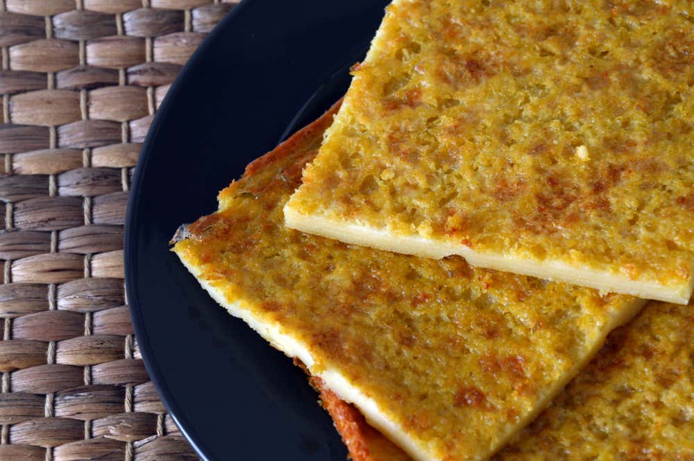 Porciones rectangulares de farinata de garbanzos bien dorada y crujiente por encima, servidas en un plato negro sobre un mantel de mimbre