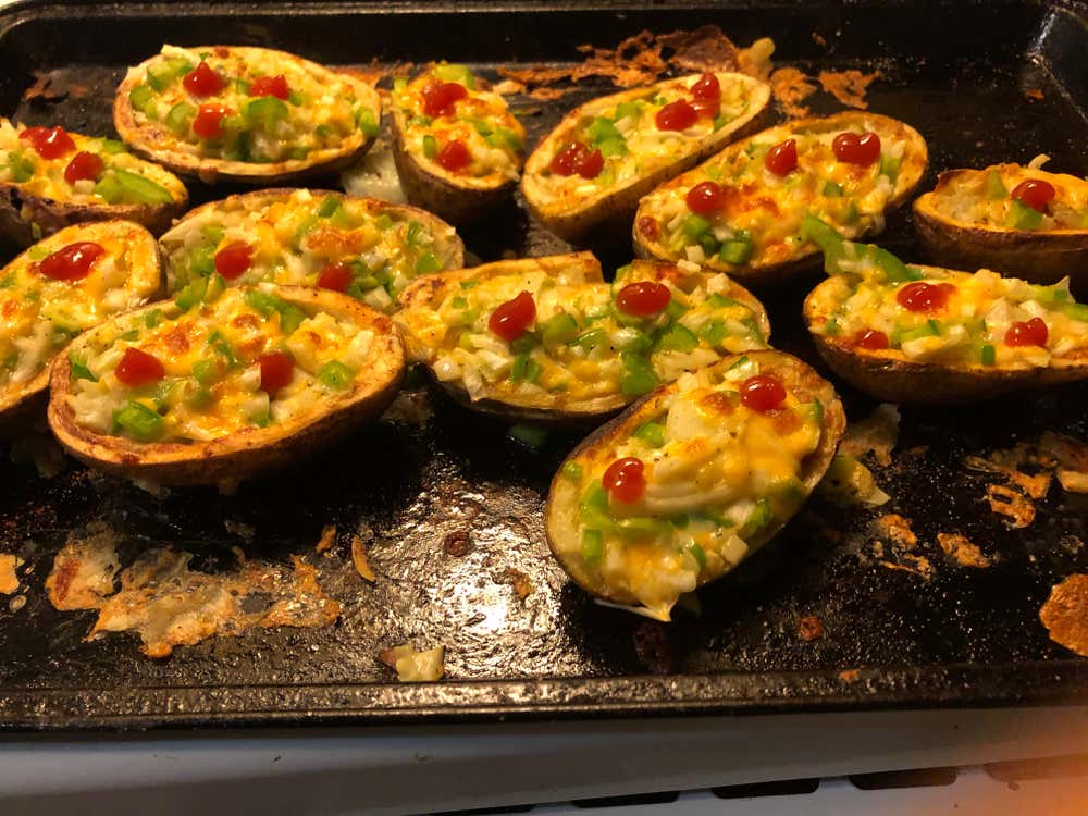 Una bandeja de horno llena de patatas asadas rellenas, con queso fundido, pimiento verde en dados y gotas de salsa roja