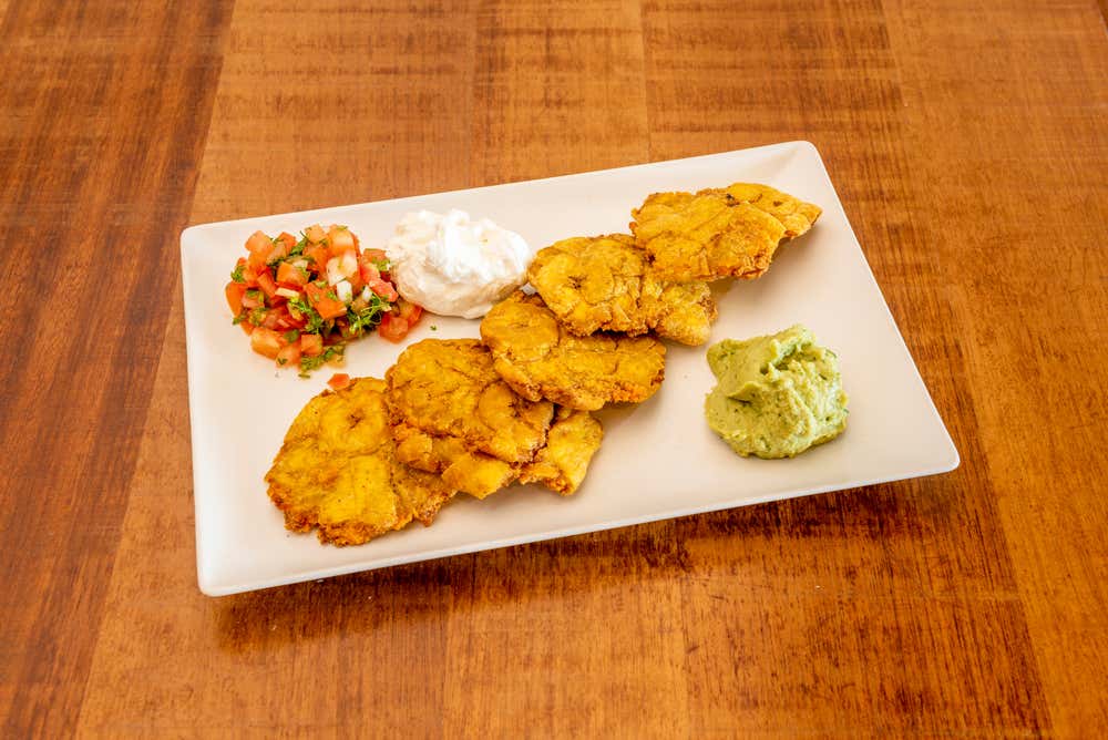 Patacones with pico de gallo, guacamole and sour cream on a white plate on a wooden table.