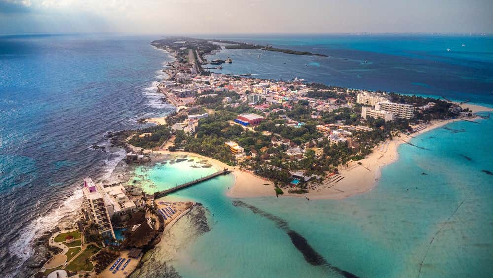 An aerial shot of Playa Norte and the Islas Mujeres, with lots of trees and buildings in sight.