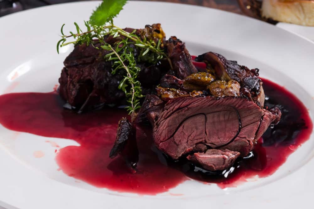 Plato elegante con tiernos trozos de brasato al Barolo bañados en una reducción de vino tinto densa y brillante, decorados con hierbas aromáticas frescas