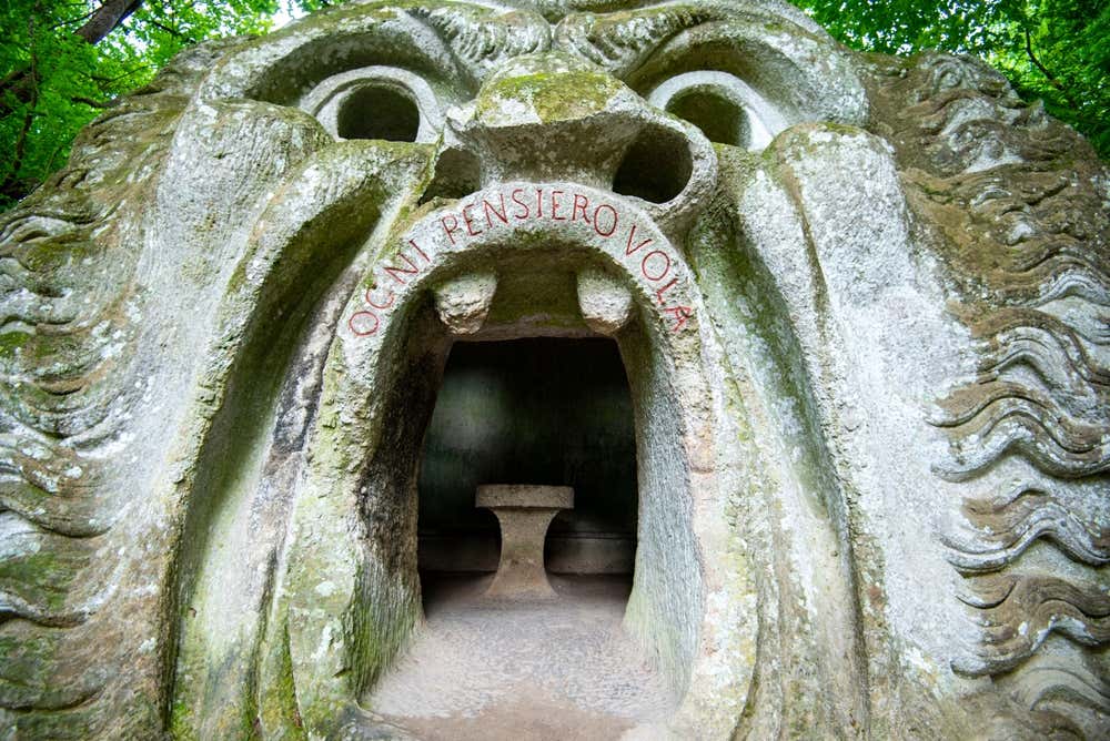 La Bocca dell'orco nel Sacro Bosco di Bomarzo: un enorme volto mostruoso scolpito nella roccia e coperto di muschio, con occhi e naso cavi. Sul labbro superiore è incisa in rosso la scritta "Ogni pensiero vola", e dentro la bocca spalancata si vede una stanza con un tavolo di pietra