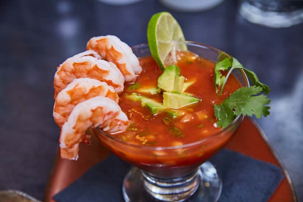 Cocktail de camarões com abacate e limão, servido em uma taça sobre a mesa de um restaurante, com os ingredientes dispostos em camadas