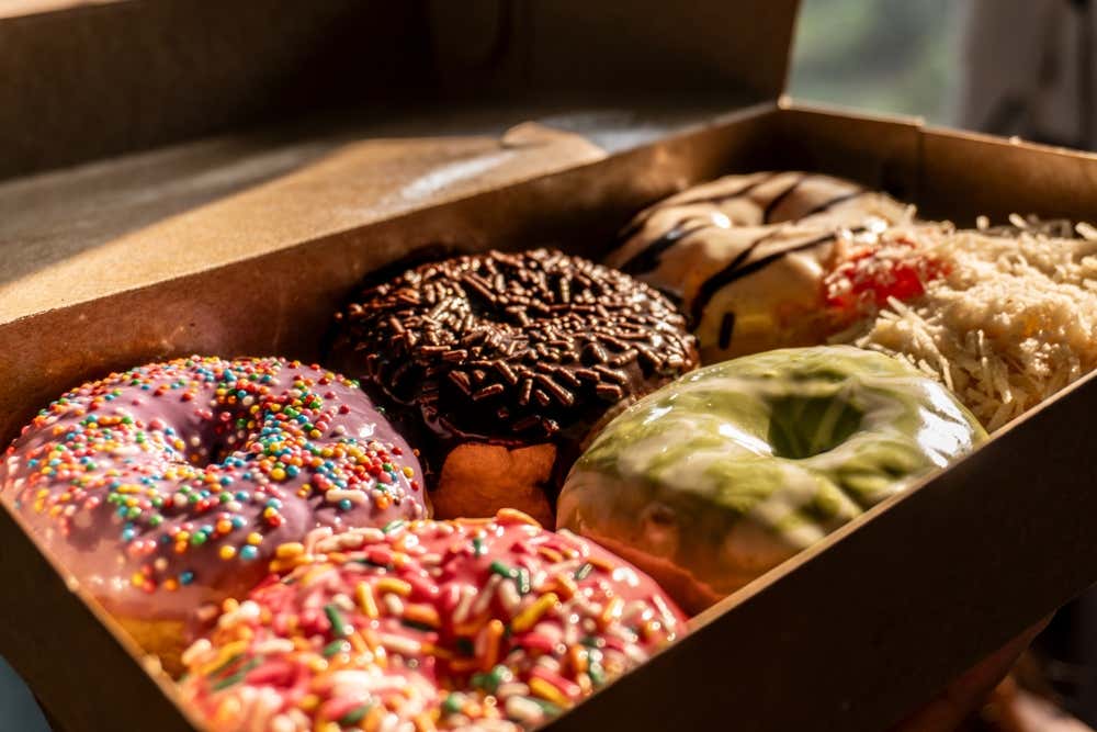 Caixa com donuts de diferentes cores e coberturas, iluminados pela luz suave do pôr do sol