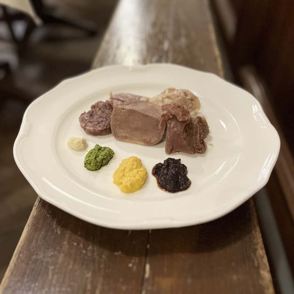 Plato blanco con cortes de bollito misto piamontés (incluida la lengua) acompañados de salsas tradicionales de colores como el bagnet verd y el bagnet ross