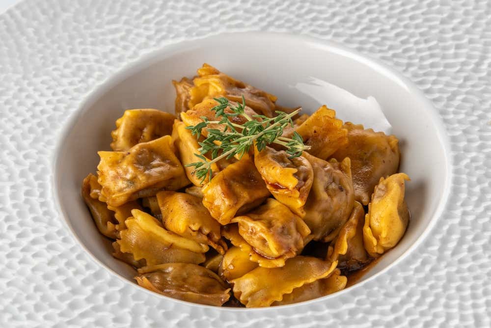 Plato hondo blanco con agnolotti del plin piamonteses aliñados con jugo de asado y decorados con una ramita de tomillo fresco