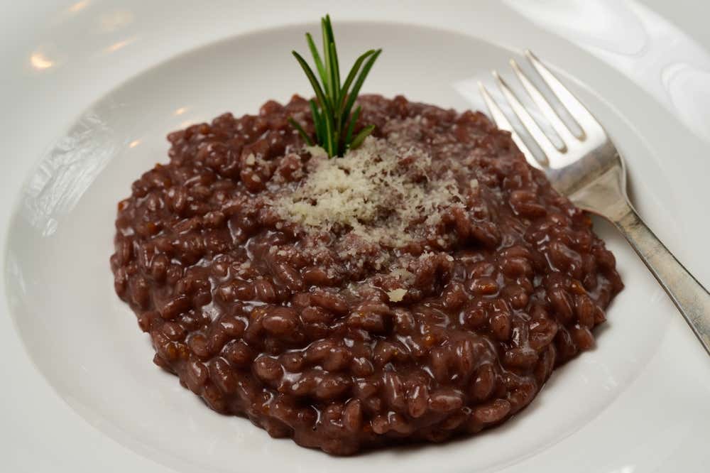 Plato de risotto al Barolo del típico color rojo oscuro, espolvoreado con queso rallado y decorado en el centro con una ramita de romero fresco