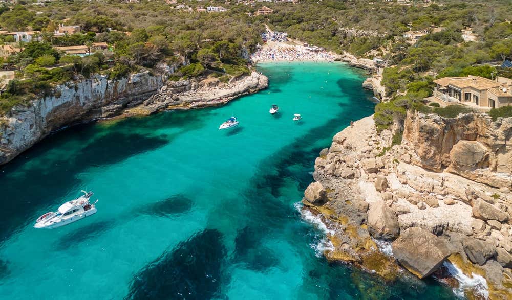 Vista aérea da Cala Llombards, em Mallorca, nas Ilhas Baleares, Espanha, com a praia de areia branca cercada por falésias e as águas azul-turquesa do Mar Mediterrâneo