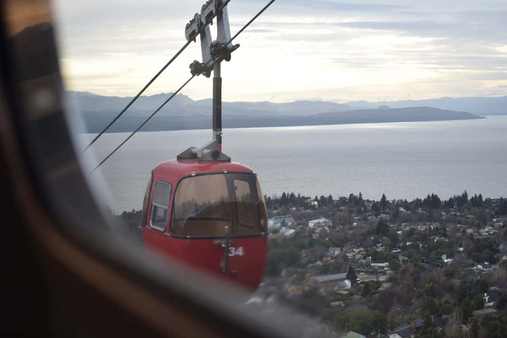 Teleférico vermelho subindo o Cerro Otto, em Bariloche, cercado por uma paisagem montanhosa
