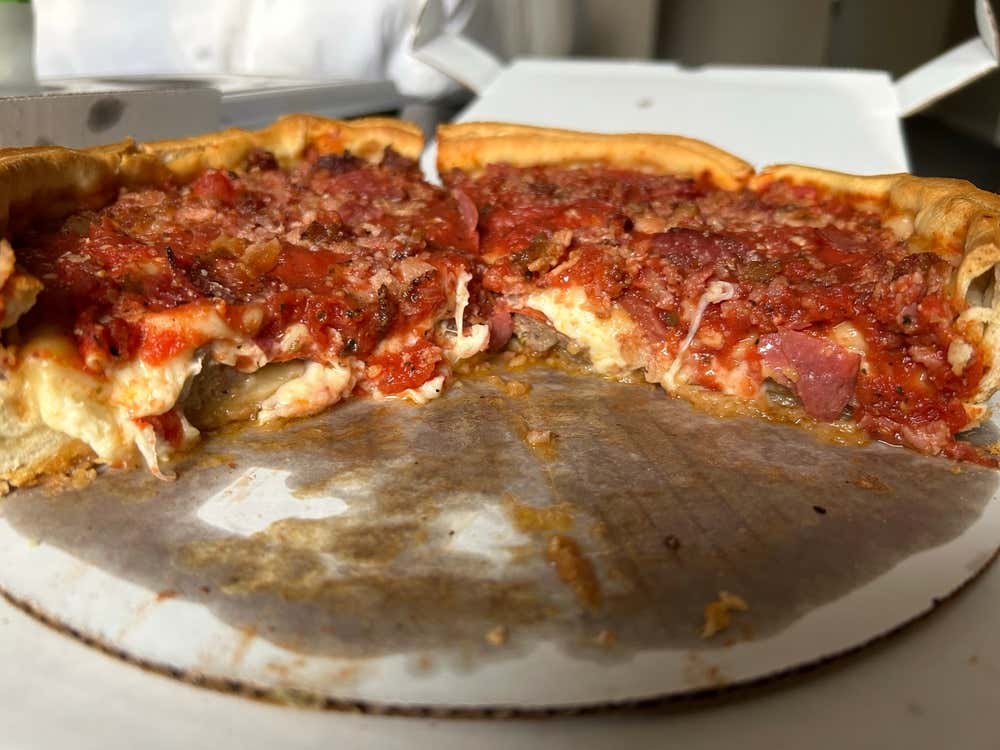 A shot of just over half of a Chicago deep dish pizza ona a circular piece of cardboard stained with grease.
