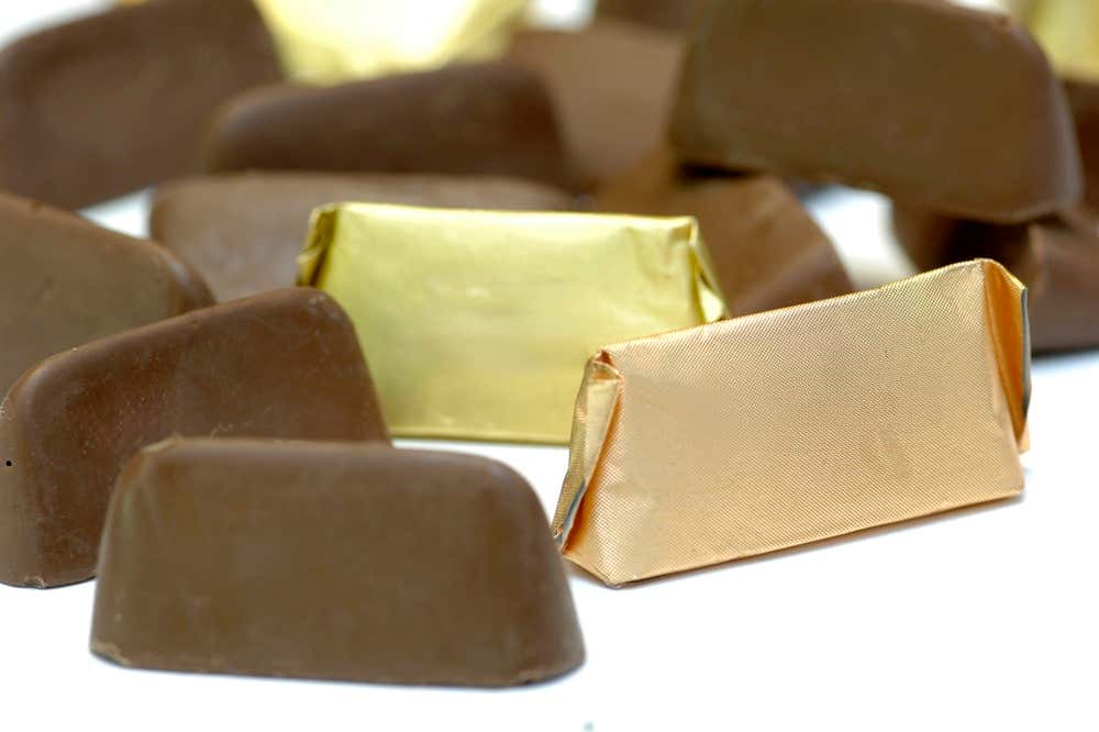 Gianduiotti clásicos con forma de barca invertida, algunos envueltos en el típico papel dorado y otros de chocolate gianduia al descubierto sobre un fondo blanco