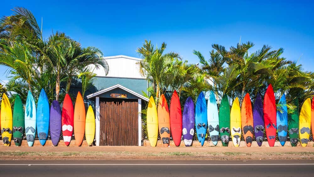 A selection of differently colored surf boards borders a building with a wooden door.