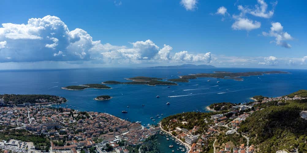 pettacolare panoramica aerea della città costiera di Hvar (Lesina) e dell'arcipelago delle Isole Pakleni (Pakleni Otoci) sparse nel mare blu intenso sotto un cielo azzurro con nuvole bianche