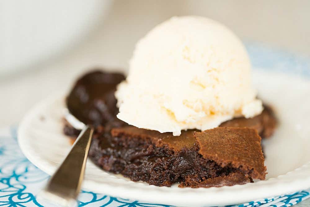 A brownie on a plate with a scoop of icecream and a spoon.