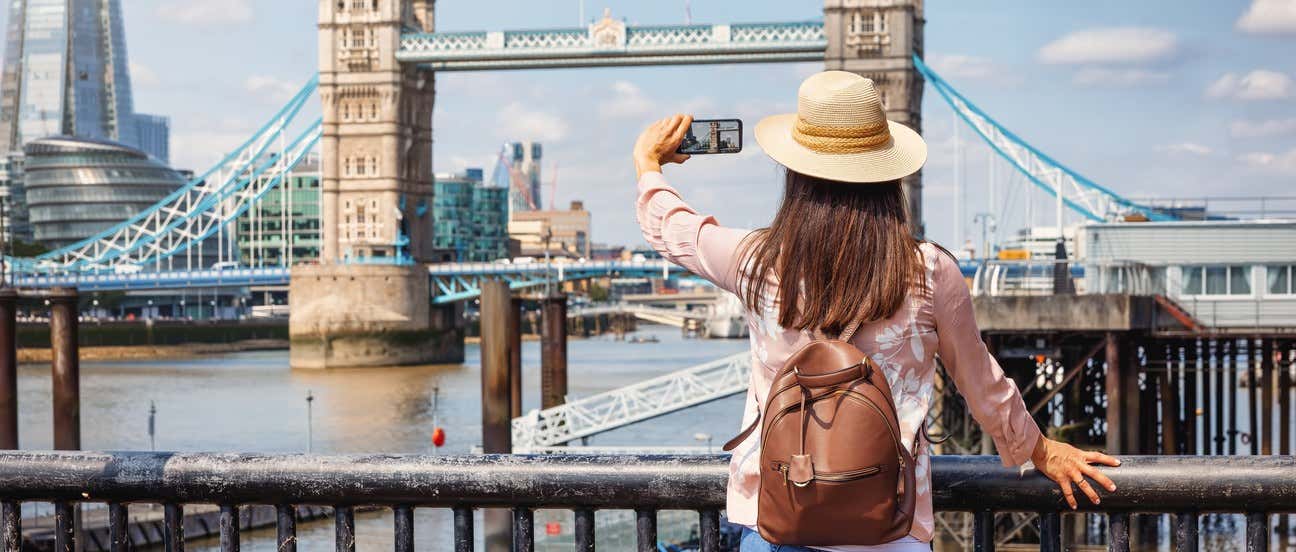 Mulher tirando uma foto com o celular em frente à Tower Bridge e ao Shard, em Londres