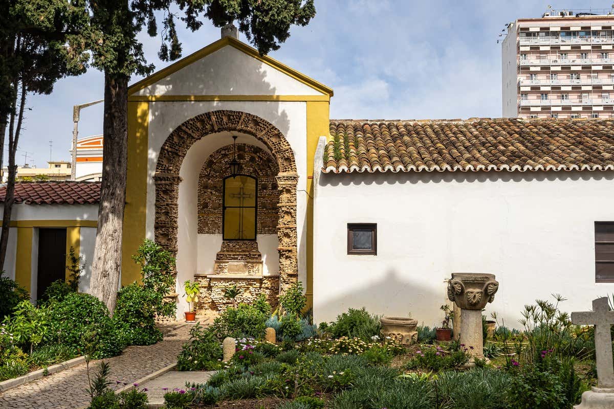 Capilla encalada con arco de piedra decorada y jardín con plantas en Faro