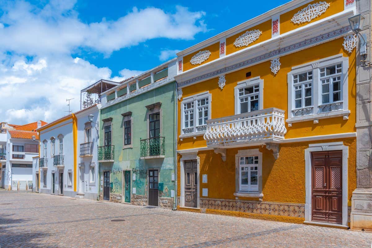 Casas de fachadas amarillas, verdes y blancas con balcones en una calle empedrada de Tavira