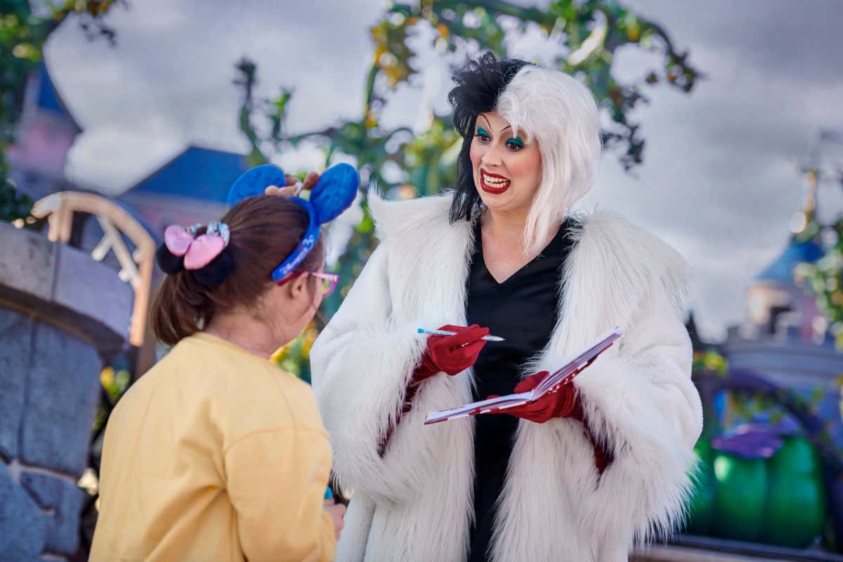 Una mujer vestida de Cruella de Vil firma un autógrafo a una niña en el parque Disneyland® Paris