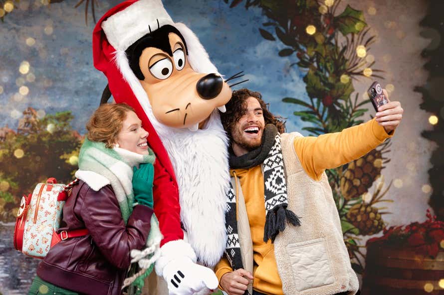 Visitantes sonrientes tomándose una foto junto a Goofy vestido con traje de Papá Noel
