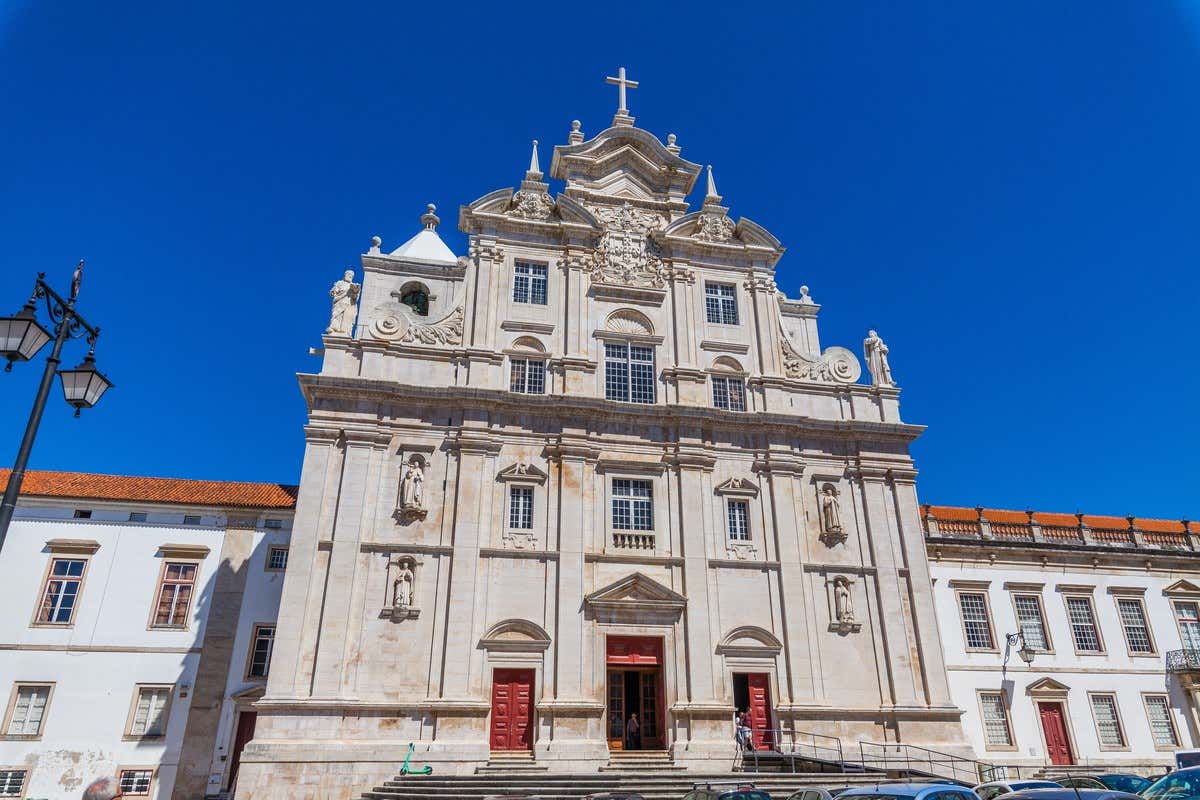 Fachada barroca da Sé Nova de Coimbra com esculturas e portas vermelhas sob céu azul