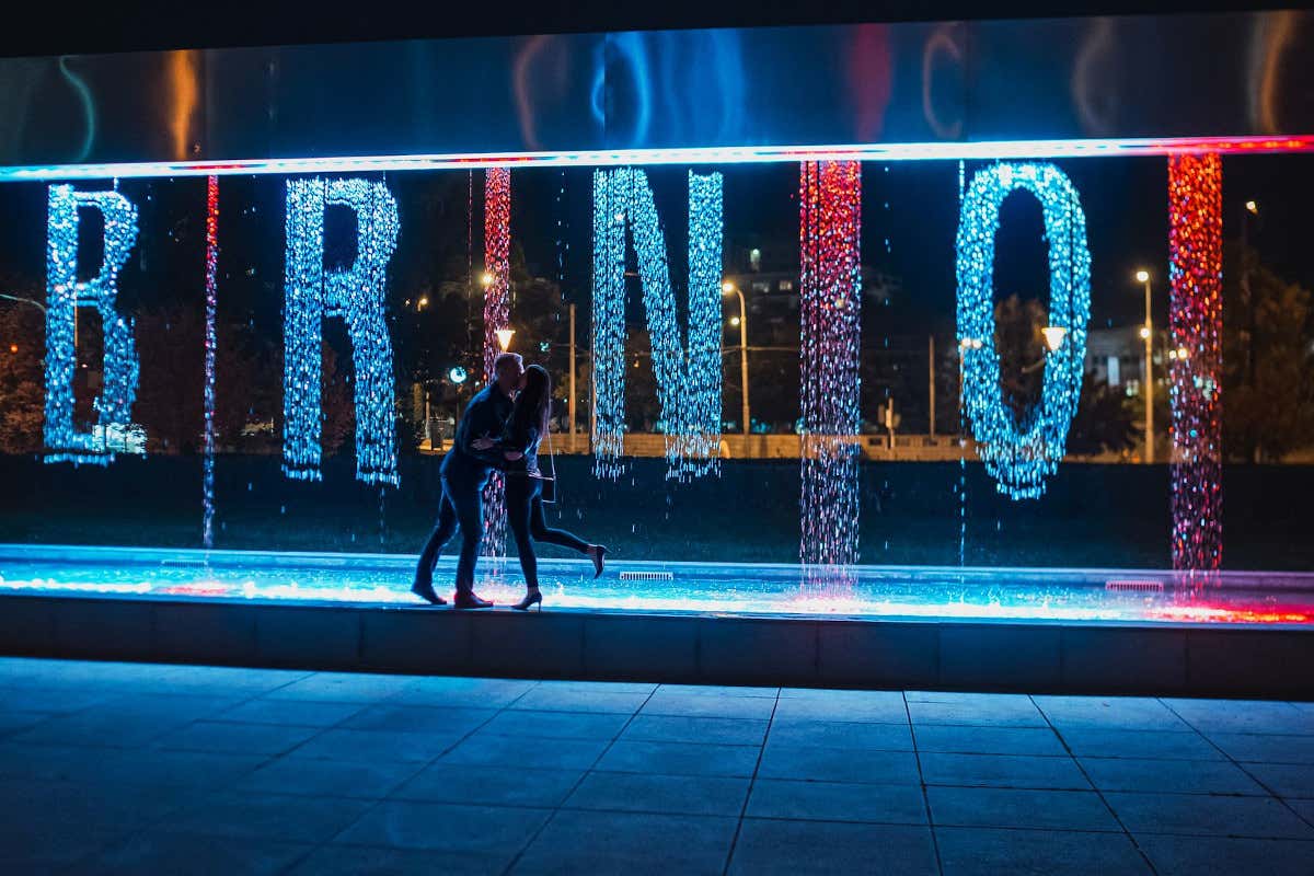 Una pareja se besa de noche frente a un letrero iluminado que pone Brno