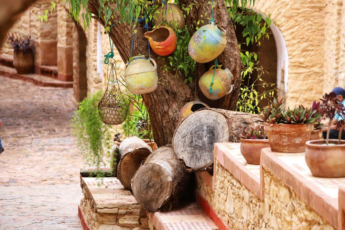 Vasijas de cerámica colgadas de un árbol en patio con macetas de barro