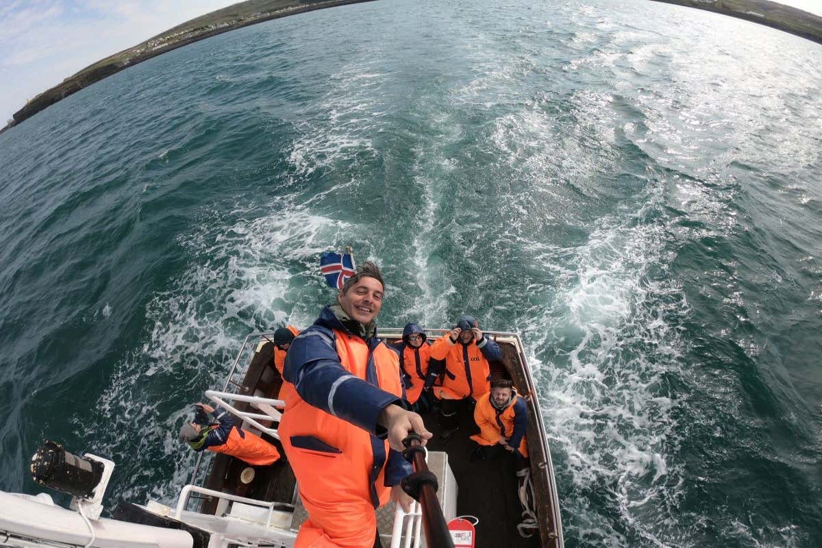 Un hombre sacando un selfie en una barco junto a otras personas mientras navegan en el mar.