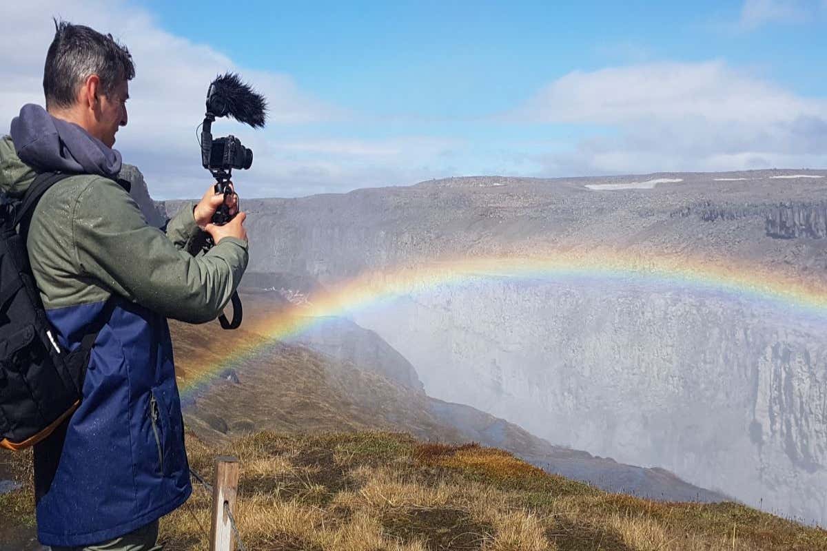Un hombre sacando una foto de la cascada Dettifoss en Islandia con un arcoiris.