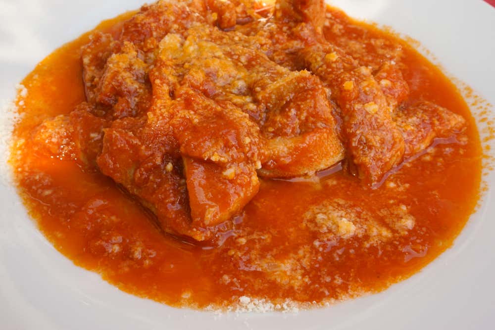 Un piatto fondo bianco con trippa alla romana in abbondante sugo di pomodoro, spolverata di pecorino grattugiato