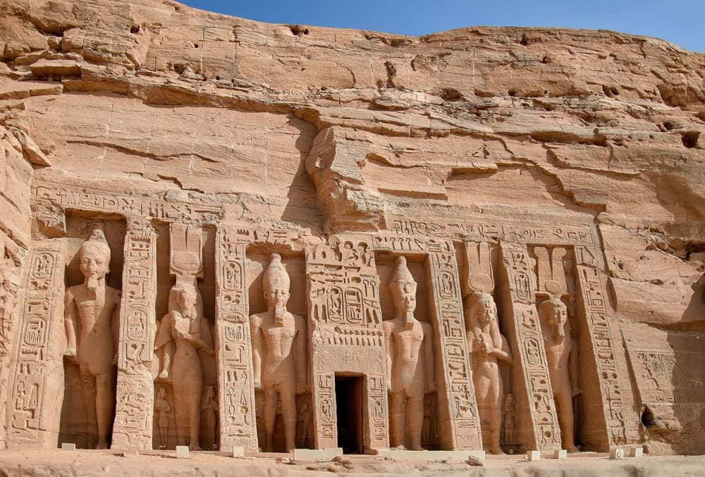La facciata del tempio minore di Abu Simbel, dedicato a Nefertari e alla dea Hathor, scavata nella roccia arenaria. Sei grandi statue in piedi, di Ramses II e della regina Nefertari, sono separate da pilastri coperti di geroglifici. Al centro si apre l'ingresso del tempio