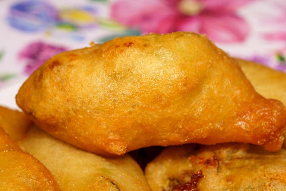 Primo piano di fiori di zucca fritti in pastella, dorati e croccanti, impilati su una tovaglia a fiori rosa e viola