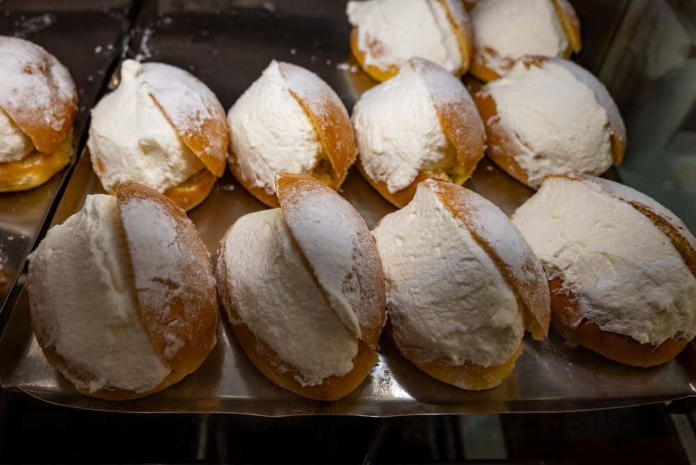Una teglia di maritozzi con la panna nella vetrina di una pasticceria: panini dolci e dorati, tagliati a metà e riempiti di panna montata, con una spolverata di zucchero a velo