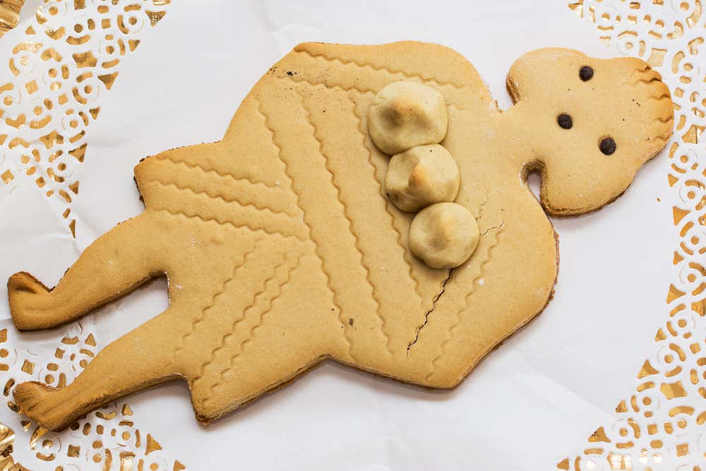 La pupazza frascatana, un biscotto al miele a forma di donna con tre seni rotondi, gli occhi di cioccolato e decorazioni ondulate sul corpo, appoggiato su un centrino di carta bianco e oro