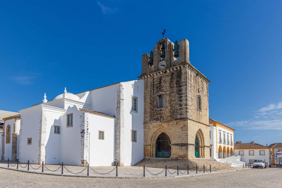 Torre campanario de piedra de la Sé de Faro junto a fachadas blancas bajo cielo azul
