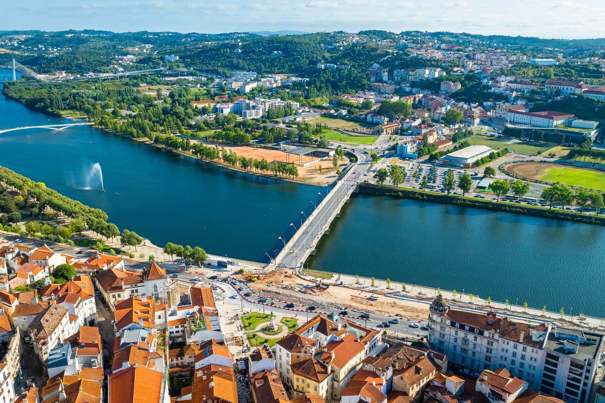 Vista aérea de Coimbra com o rio Mondego, uma ponte e o centro histórico em primeiro plano