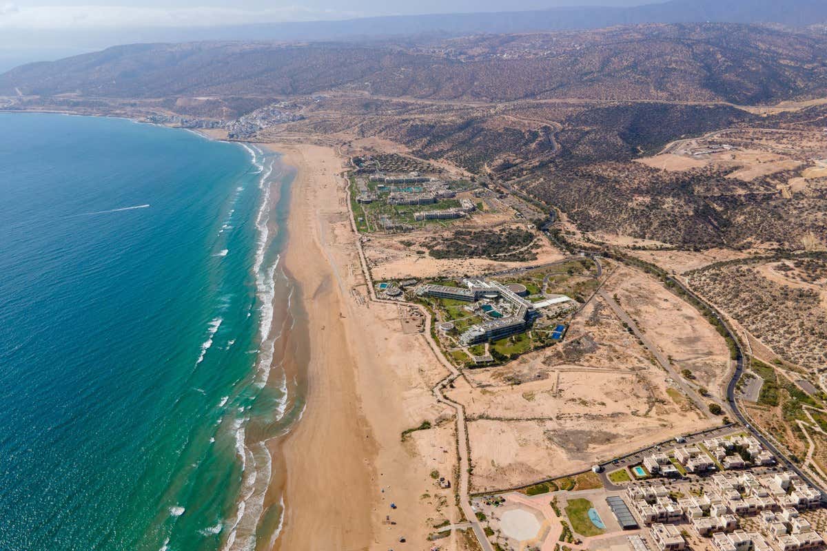 Vista aérea de la playa de Agadir con hoteles junto al mar y montañas al fondo