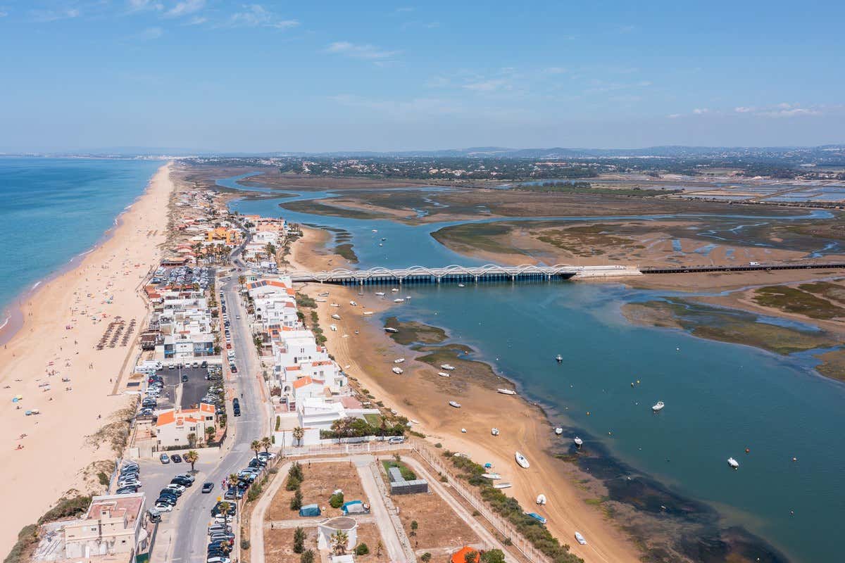 Vista aérea de la praia de Faro con su larga playa de arena, casas blancas y un puente sobre la ría