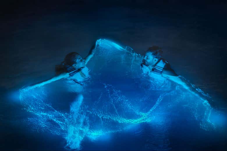 Una pareja nadando con chalecos salvavidas al caer la noche