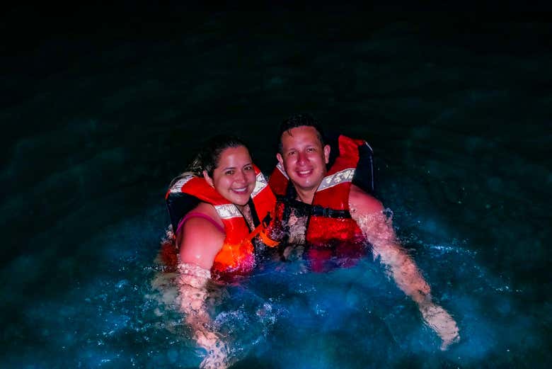 Una pareja nadando con chalecos salvavidas al caer la noche
