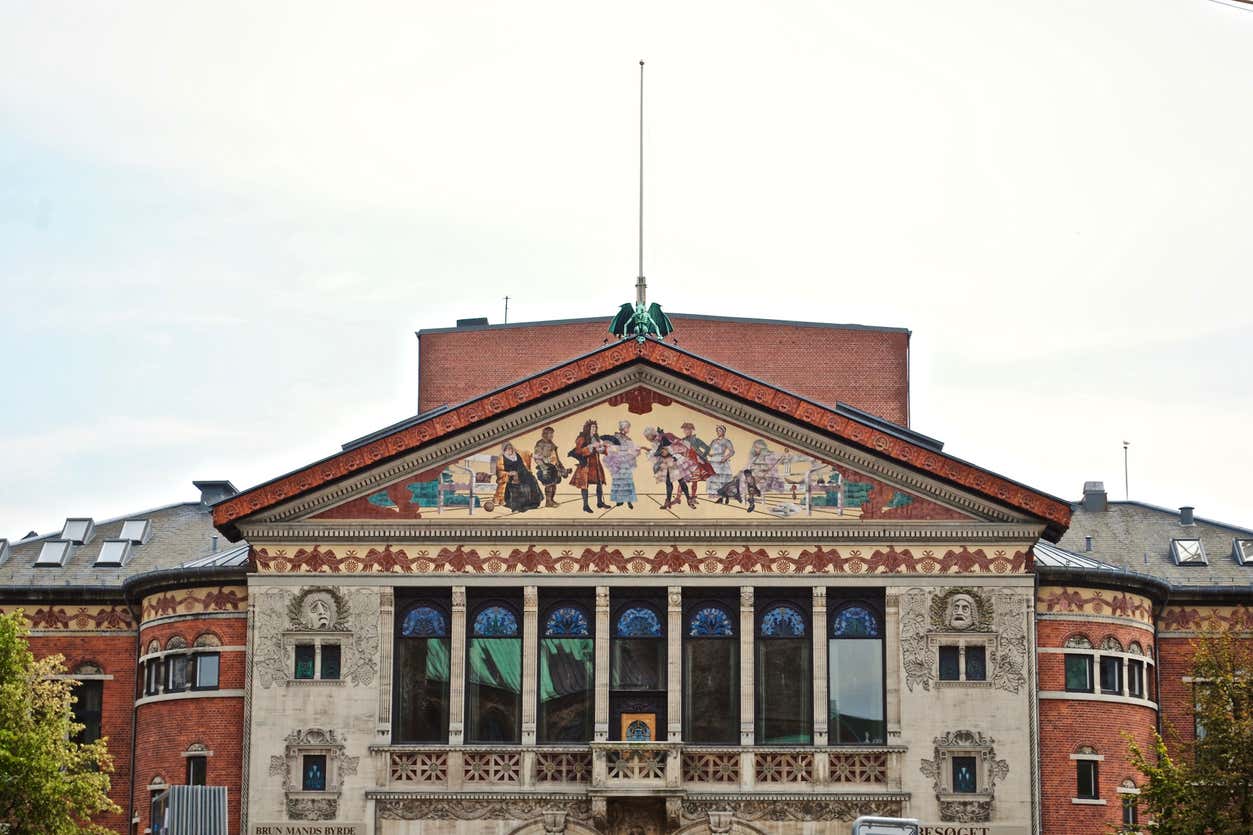 Teatro de Aarhus, edifício quadrado com teto triangular. No centro do triângulo, há pintura de pessoas vestidas como na era vitoriana, para representar Dinamarca.