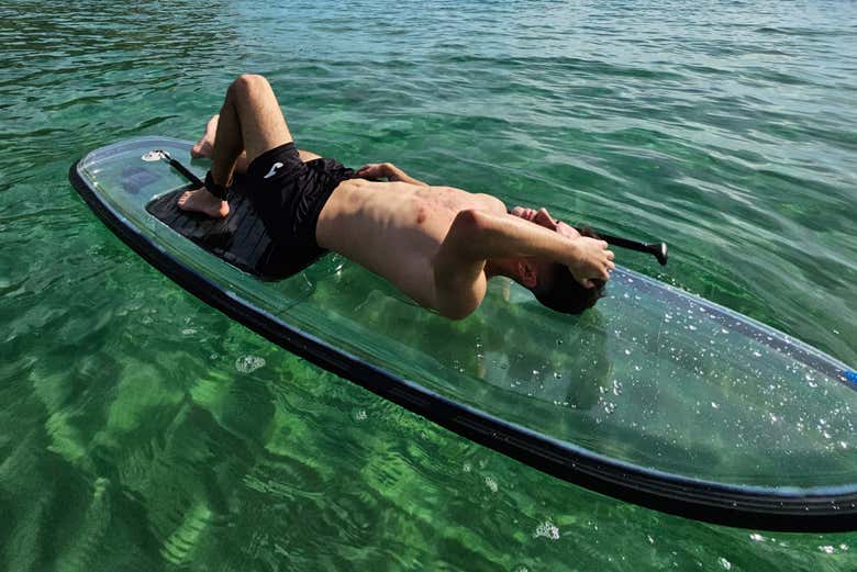 Un chico tumbado sobre la table de paddle surf transparente