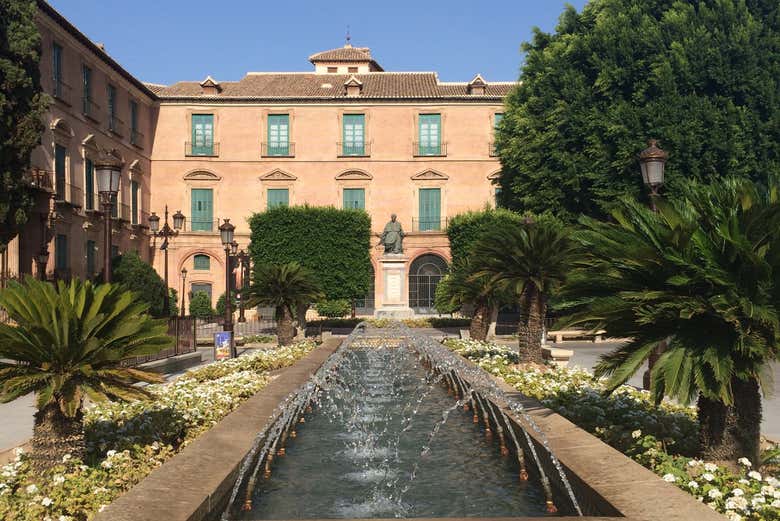 Una fuente rodeada de plantas y árboles con un edificio al fondo