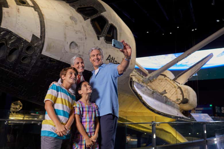Família tirando uma selfie ao lado de um ônibus espacial