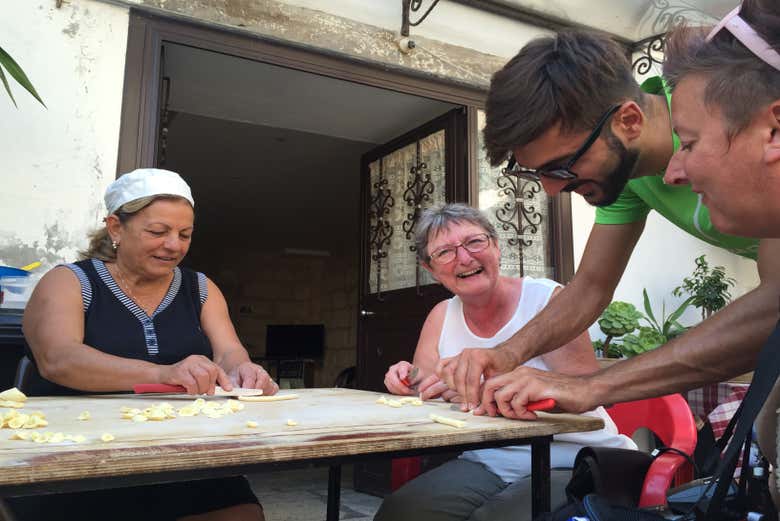 Signora che prepara le orecchiette in compagnia di due turisti