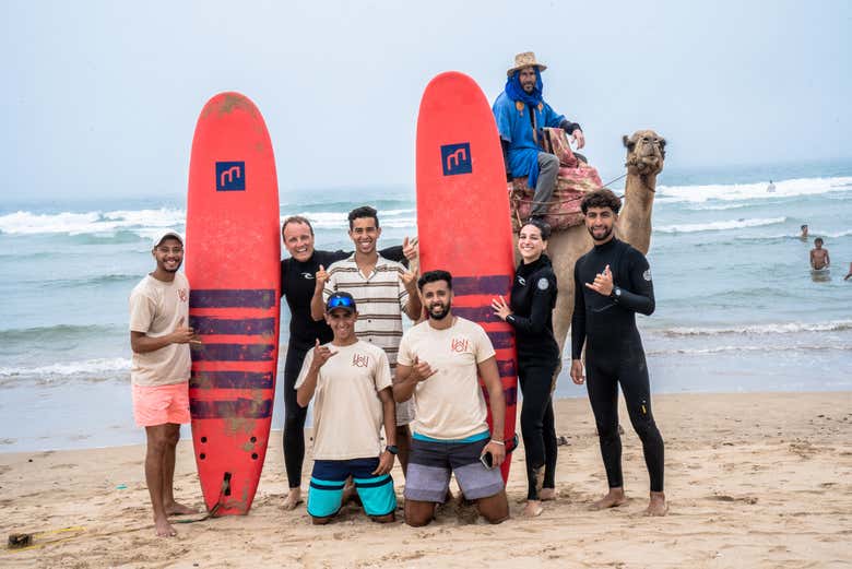 Groupe de surfeurs avec un local à dos de chameau sur la plage