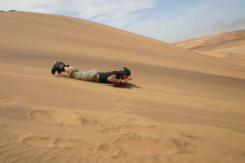 Hombre haciendo sandboarding en la modalidad lie down