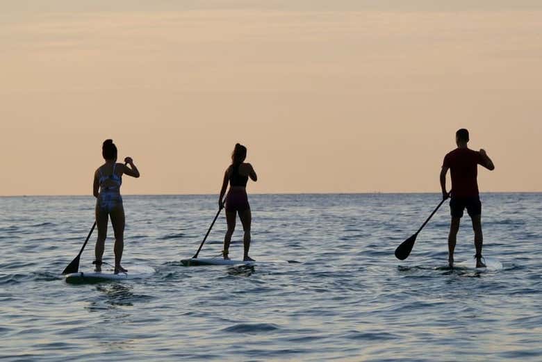 Tres personas haciendo paddle surf al atardecer